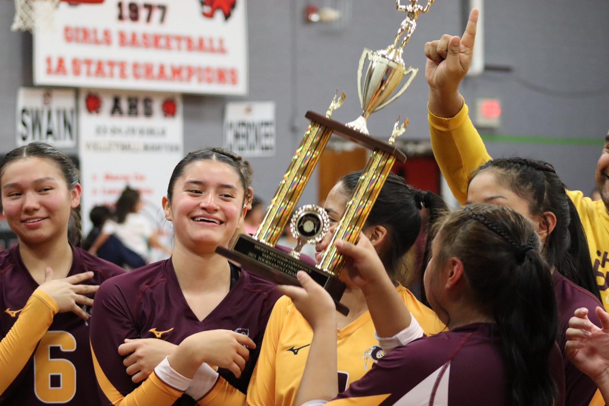 A group of the Lady Braves wearing maroon and gold uniforms hold up their trophy after winning the 2023-24 SMC Tournament Championship