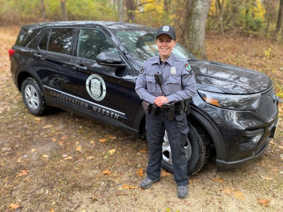 A DNR warden standing in front of a conservation warden vehicle