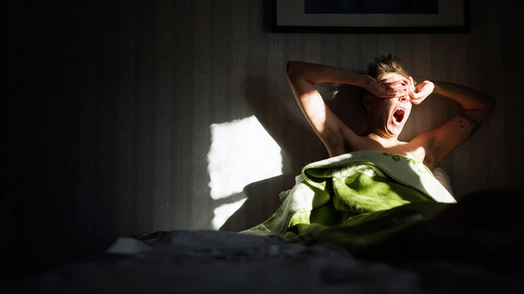 A person yawning in bed and rubbing their dry eyes.-1