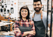 Foto: Dueños de negocios hispanos - Una mujer y un hombre en delantales de trabajo con tienda detrás de ellos.