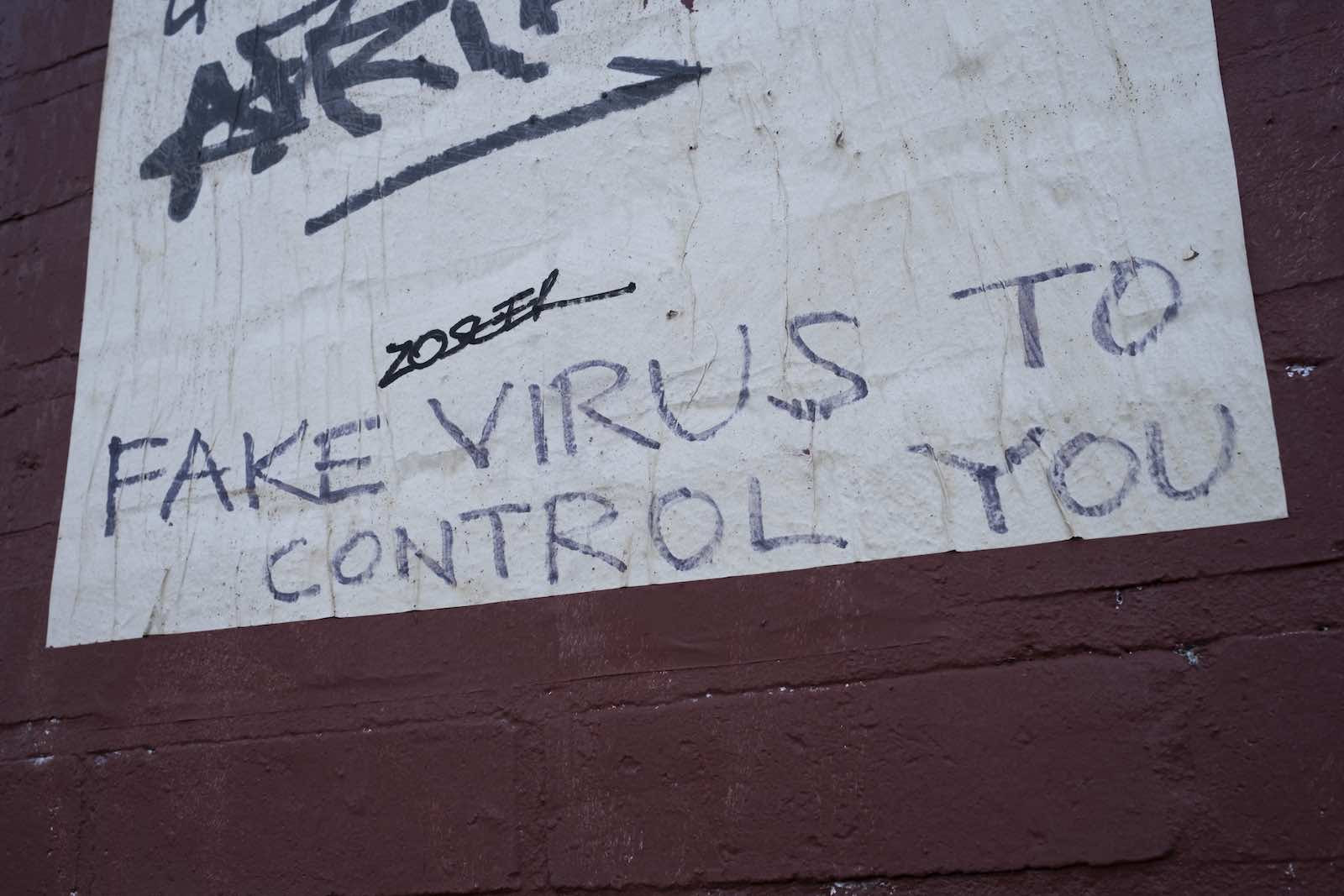 Graffiti on the side of a building that says “fake virus to control you”