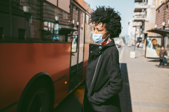 Woman at bus stop wearing face covering.