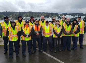 Fourteen people in safety vests posing for a photo in front of ferries