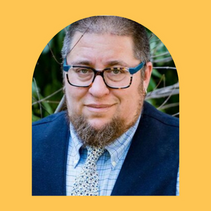 Bear Bergman, a white, trans Jewish man, wearing glasses and a suit and looking at the camera.