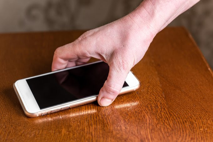 A hand is picking up a cell phone from a table.
