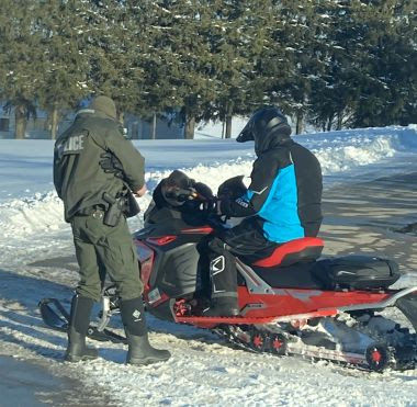 Forest Ranger inspects snowmobile a person is sitting on