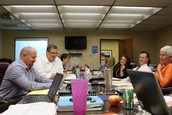 WDE staff sit at a conference table talking and laughing.