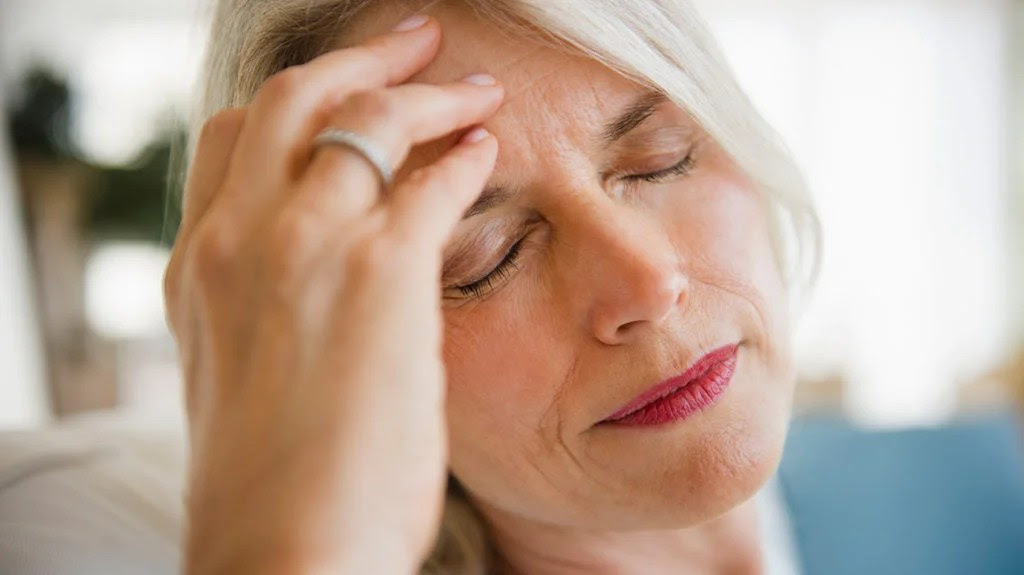 a woman holding her head because she has a headache from mono contagious and she is wondering how long is it going to last for