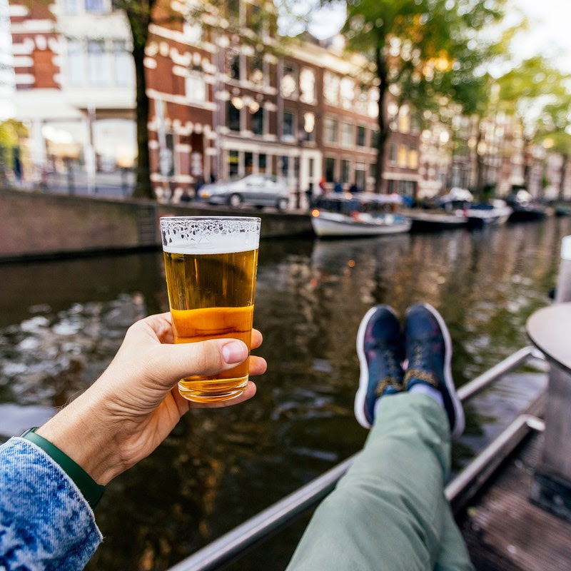 A person holds up a beer in front of Amsterdam's canals.