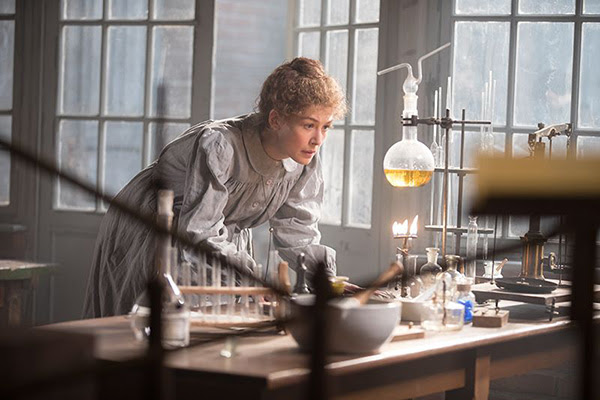 Rosamund Pike in character as Marie Curie conducts an experiment with a bunsen burner