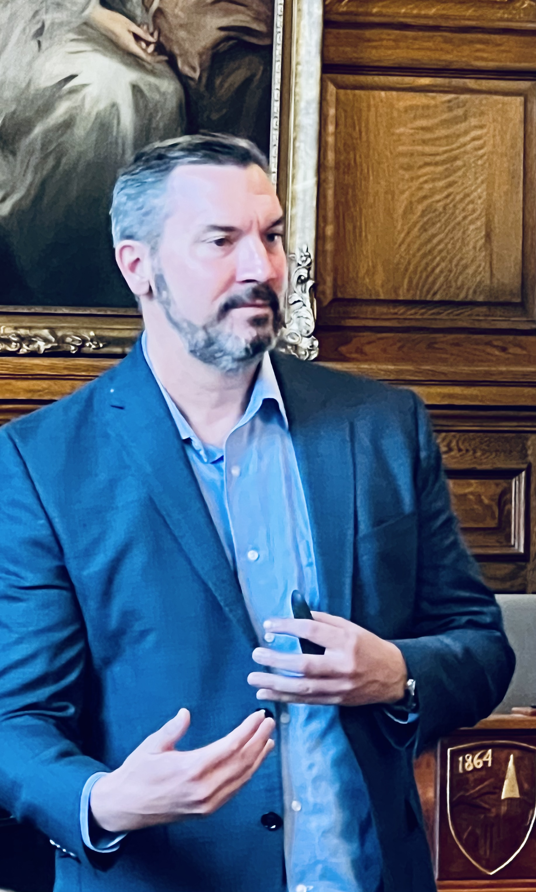 Scott Arthur is pictured presenting in a blue blazer with a thoughtful expression on his face.