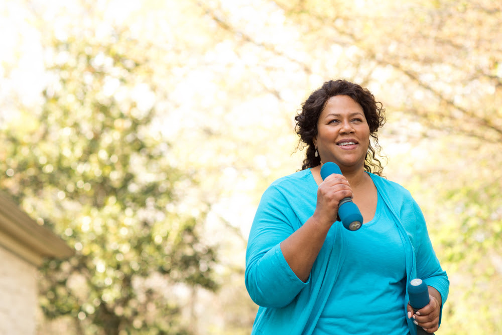african american woman in a blue sweater walking with hand weights