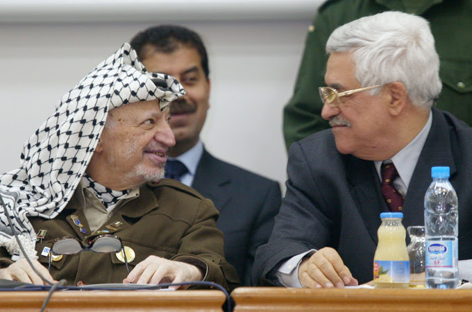 Palestinian leader Yasser Arafat and the then-incoming Prime Minister Mahmoud Abbas turn to smile at each other at a parliamentary meeting