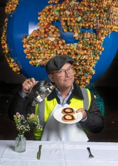 Gregg Wallace holding a plate which shows the number '8.' This is the number of meals a UK household wastes per week