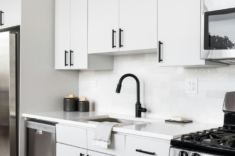 A kitchen with white cabinets and black faucet

Description automatically generated