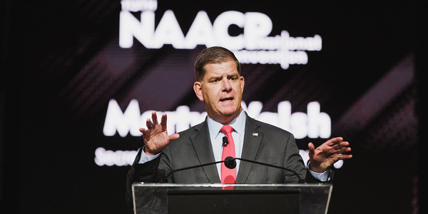 Secretary Walsh speaks from a podium bearing the NAACP logo. 