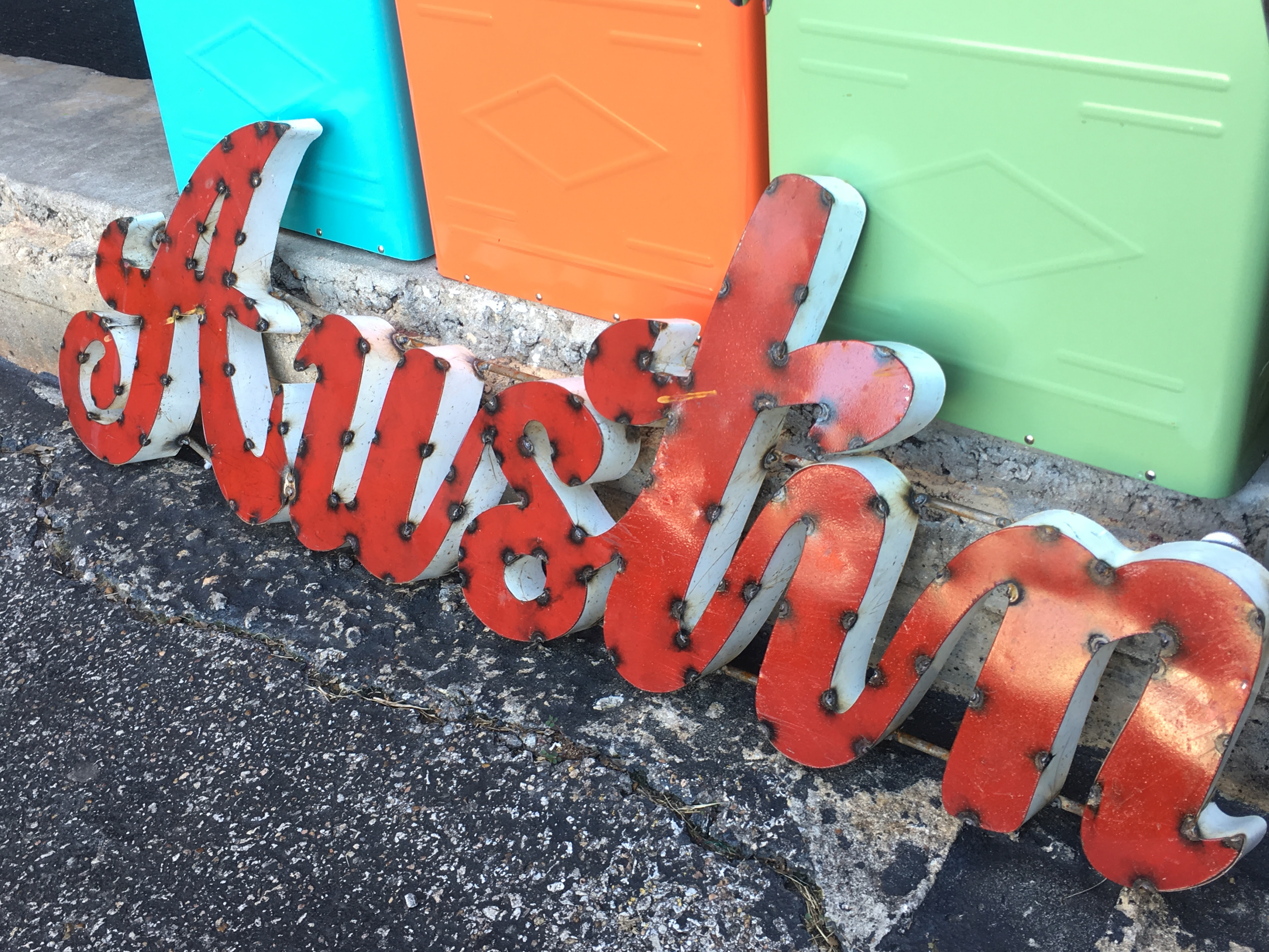 Red metal “Austin” sign with bright colors in background