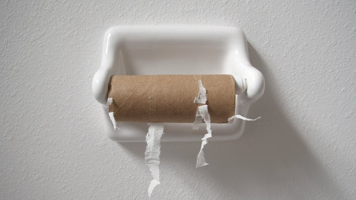 Empty toilet paper roll on the holder with a plain white wall background.