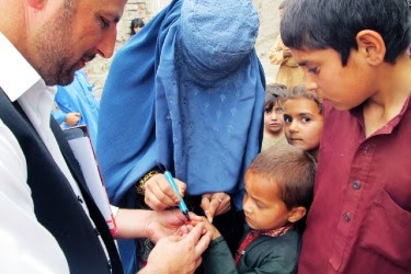 The figure is a photo of a young Afghan receiving an ink marking on his finger after vaccination to identify his vaccination status