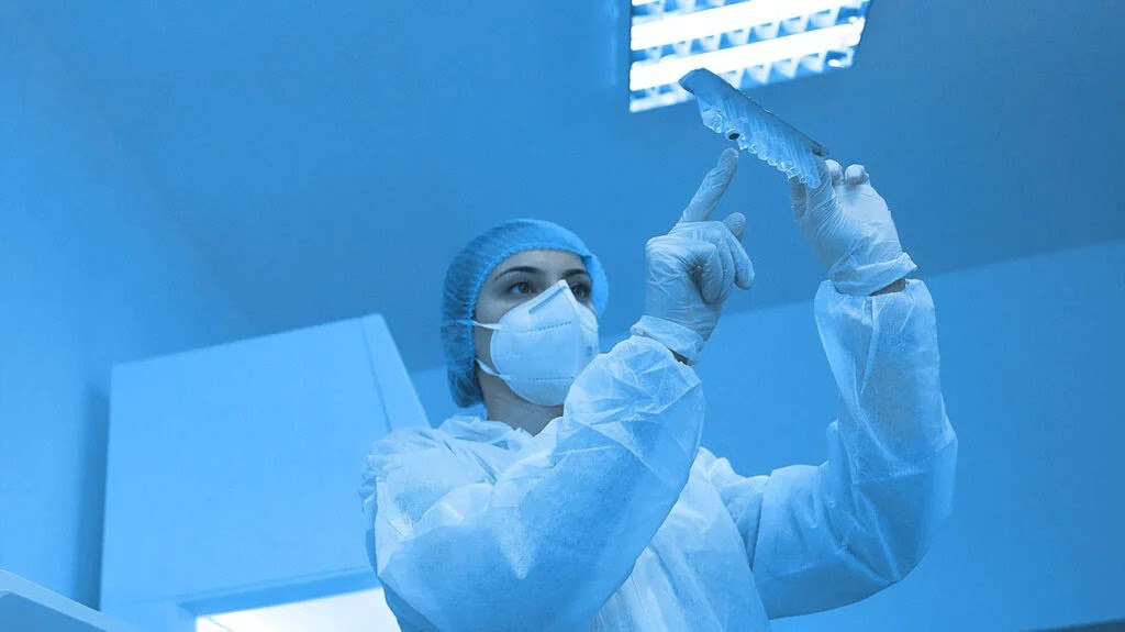 scientist in lab wearing PPE and examining lab samples