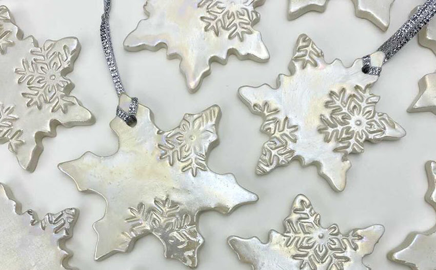 A photograph of star-shaped silver christmas ornaments. The ornaments have a shiny silver glaze on and are imprinted with snowflake motifs.