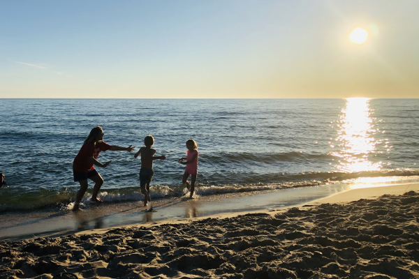 An adult and two children running in the water at Muskegon State Park beach