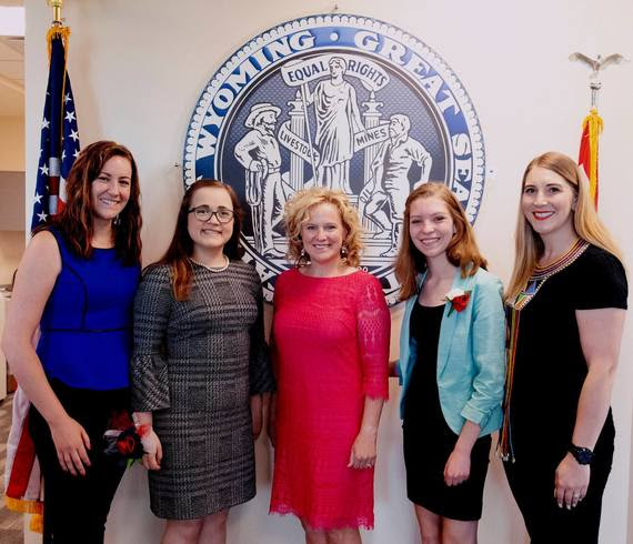 From left-to-right: WDE Communications Director Kari Eakins, Girls State delegate Riley, State Superintendent Jillian Balow, Girls State delegate Bailey, and WDE Chief Policy Officer Megan Degenfelder stand in front of the Great Seal of the State of Wyoming at the WDE.