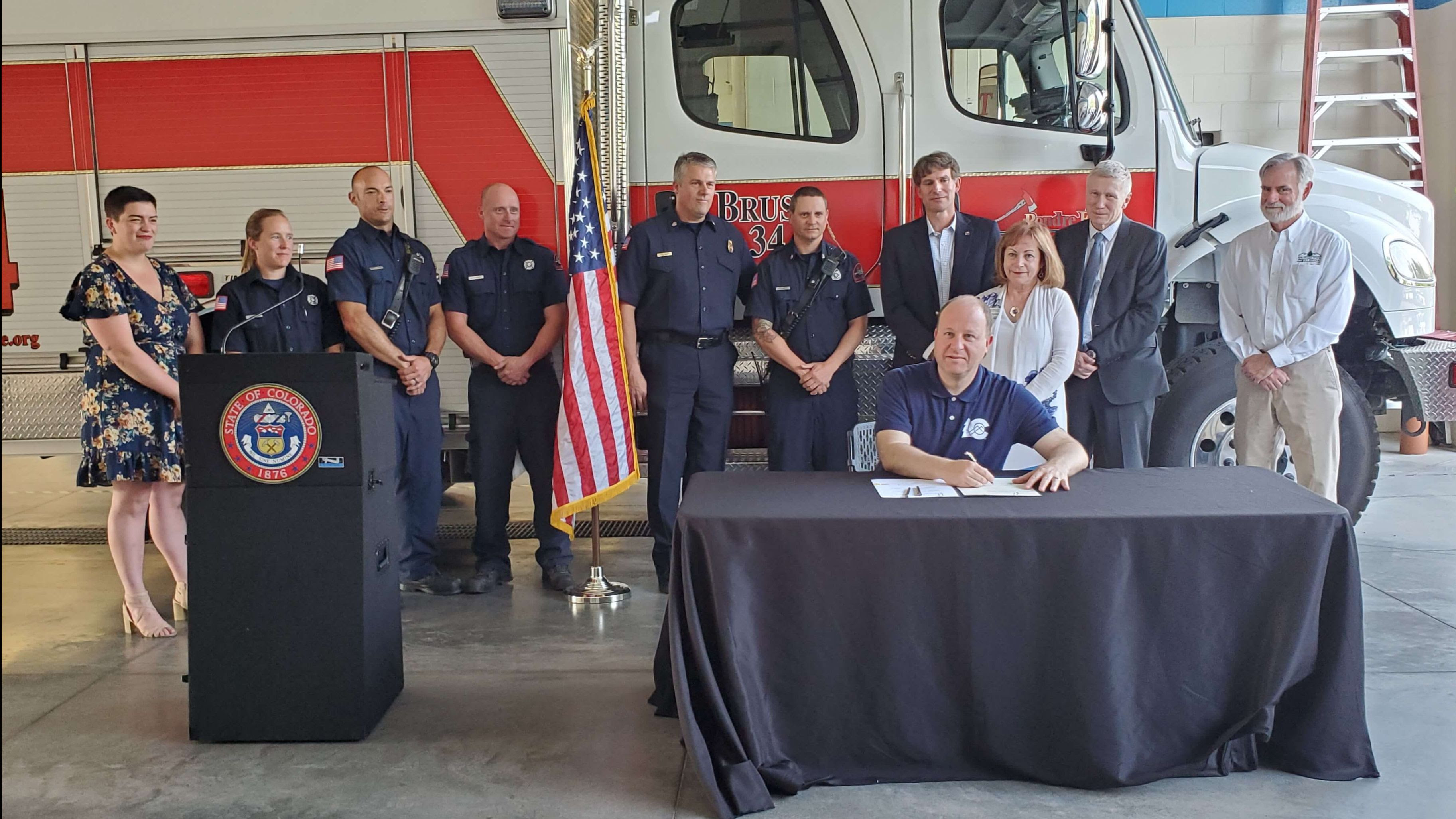 Governor signs Watershed Protection Bill at table with people and ambulance behind him
