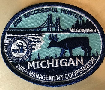 An oval-shaped, light blue patch, with dark blue imagery of the Mackinac Bridge, forest, and antlered deer. The text Mi.gov/Deer is shown.