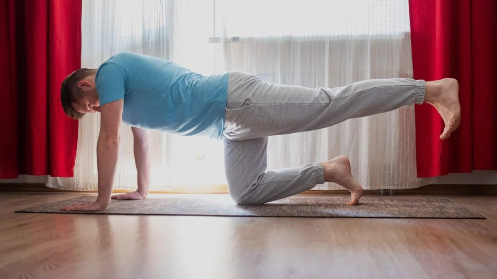 a man doing a bird dog as part of his routine of ower back stretches