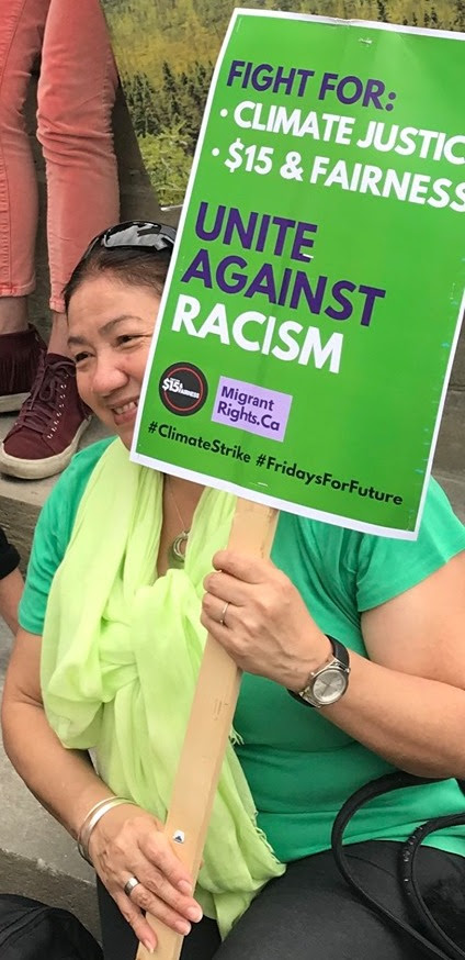 woman holds a green placard that says fight for climate and $15
& fairness, unite against racism