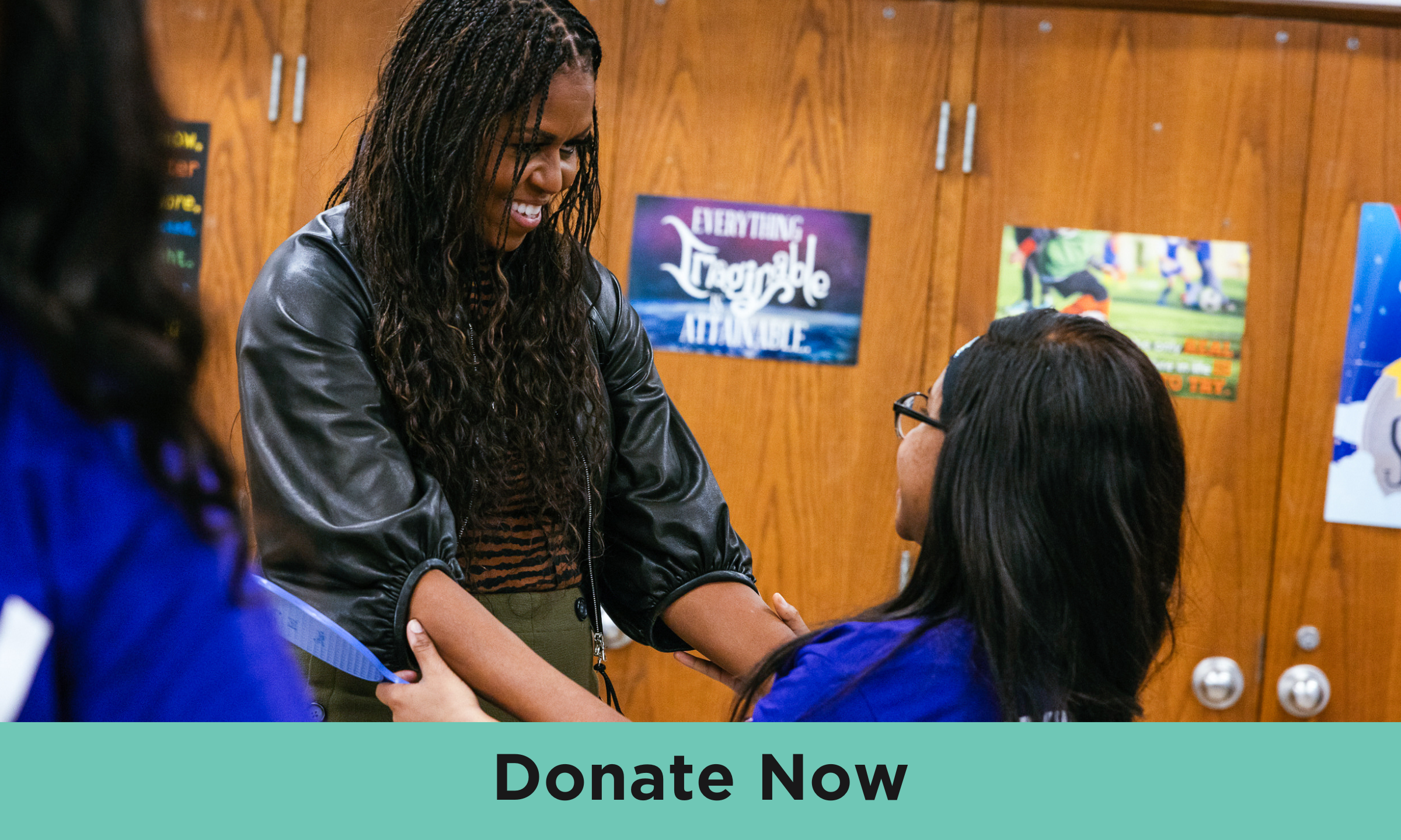Michelle Obama, wearing a black top and long braids, is reaching out and looking at a child with medium skin tone and dark, shoulder length hair. Text at the bottom says “Donate now”. 