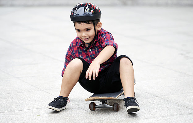 A young boy wearing a helmet sitting on a skateboard.