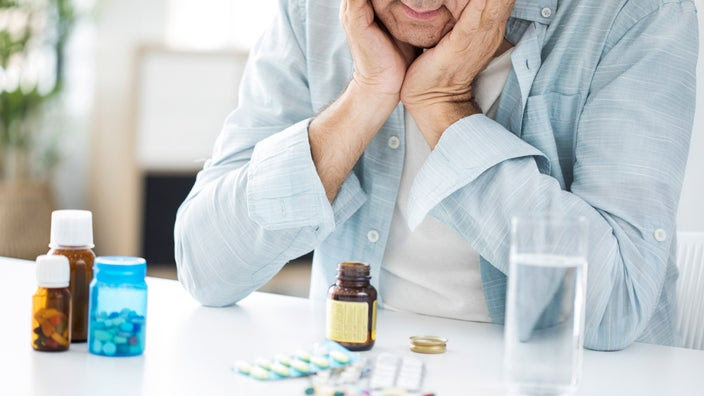 A senior man looking down at pills and thinking.