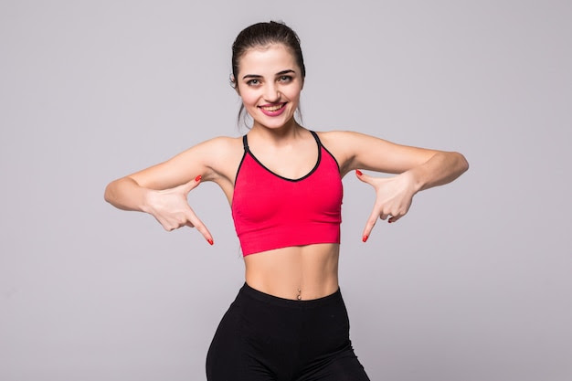 Close up of fit woman's torso pointed with her hands. female with perfect abdomen muscles on grey wall with copyspace.