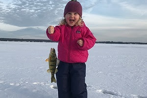 little girl ice fishing and holding up her catch