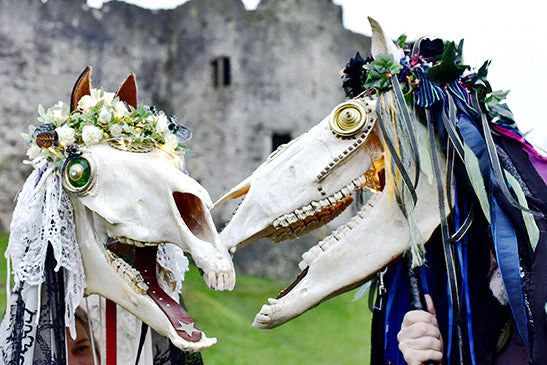 Dos personas disfrazadas de Mari Lwyd están muy contentas delante de un castillo