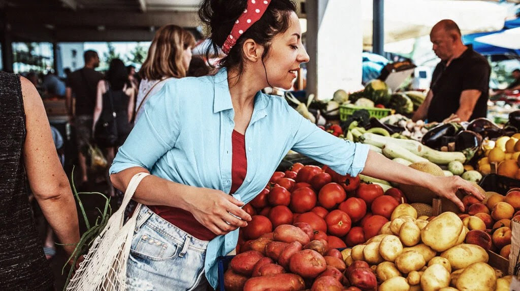 A young woman picking up fruit at a food market stall so she can follow a healthy diet.