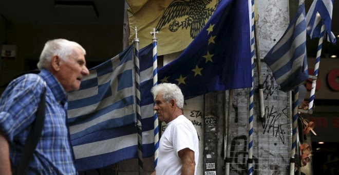 Dos hombres pasean en Atenas por delante de banderas griegas y europeas. /REUTERS