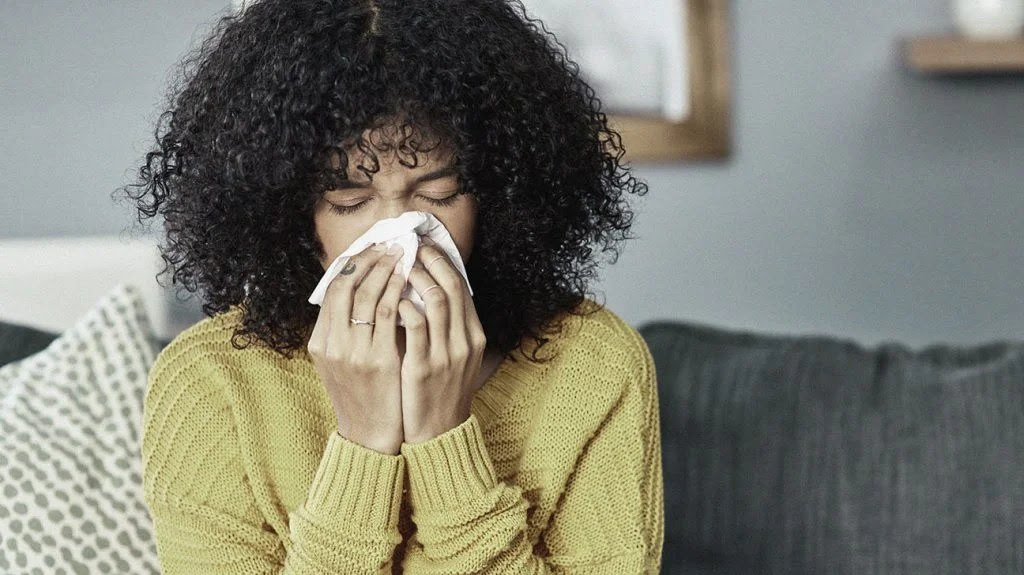 A female sneezes into a tissue due to allergies