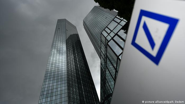 Prédio do Deutsche Bank visto de cima para baixo. Céu nublado. Logotipo do banco em primeiro plano, à esquerda. 