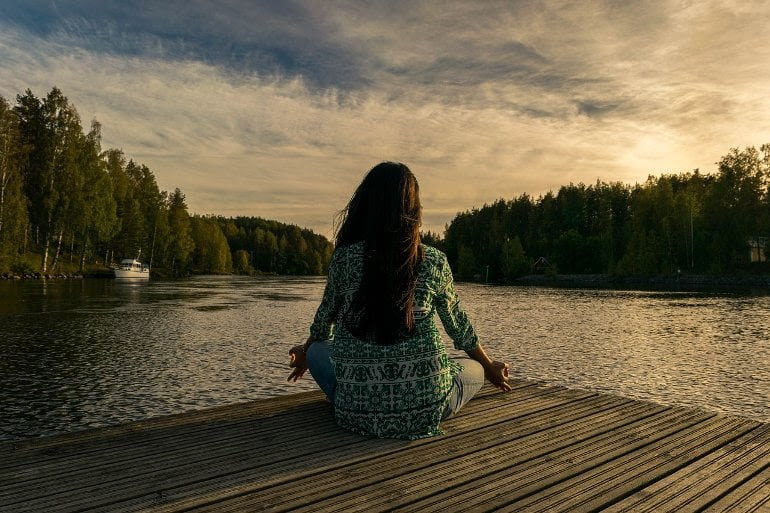 This shows a woman meditating by a lake