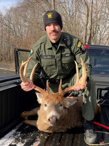 ECO holds deceased buck by antlers in back of pickup truck