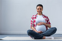 Photograph of pregnant woman sitting on the floor smiling at the camera.