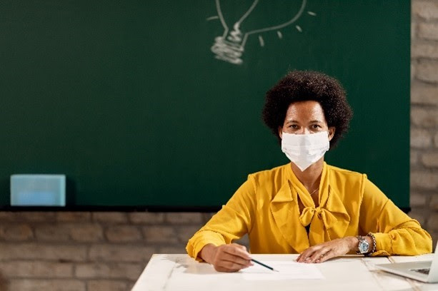 black teacher with mask at desk