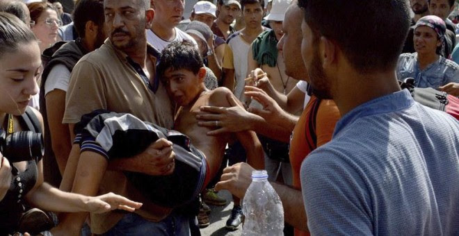 Refugiados llevan en brazos a un niño que se desmayó durante la larga espera para el procedimiento de registro en la isla griega de Lesbos. - EFE