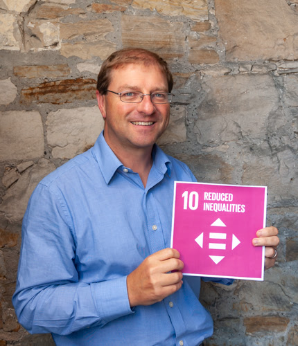 Photo of Paul, a white man in a blue shirt with glasses, holding up a sign that reads '10 - Reduced Inequalities'