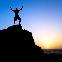 person standing on mountain top with arms raised at sunset
