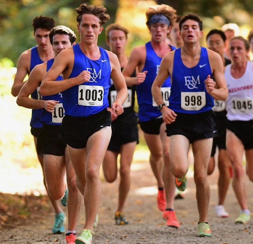 Franklin & Marshall College male runners in bright blue running singlets run towards the camera on a dirt road.