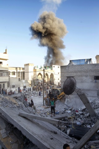 Black smoke acsends in the background from an Israeli air strike as Palestinians clear the rubble of the Ghanam family home after it was also targetted in an air raid on Rafah, in the southern of Gaza strip.  Five Palestinians, including a woman and seven-year-old child, died when the militant's house in Rafah in southern Gaza was hit, and 15 other people were wounded, Gaza emergency services spokesman Ashraf al-Qudra said.